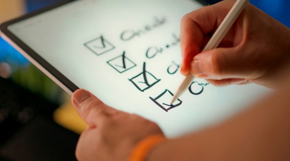 A hand ticking checkboxes on a tablet screen with a stylus