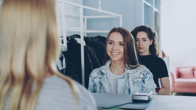 Two young women shopping and interacting with cashier