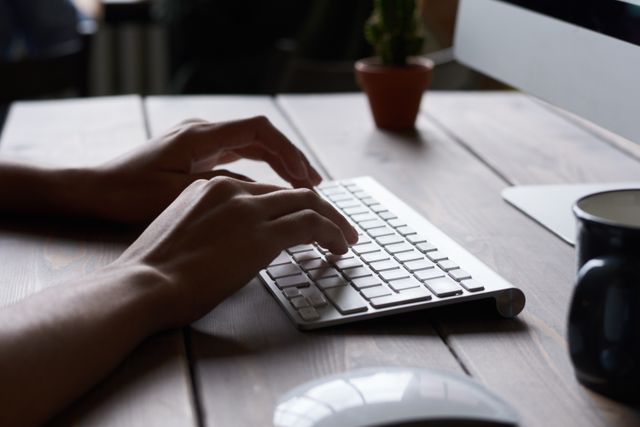 Close up of hands typing on a wireless keyboard in a modern workspace.